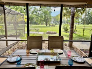 An outdoor dining area with a table set for two, overlooking a park with trees and a picnic table. - Private Pool • Game Room • Fire Pit • Boat Parking (Crystal River)