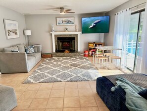 A living room with a fireplace, a television, a sofa, a coffee table, and a view through a glass door. - Private Pool • Game Room • Fire Pit • Boat Parking (Crystal River)