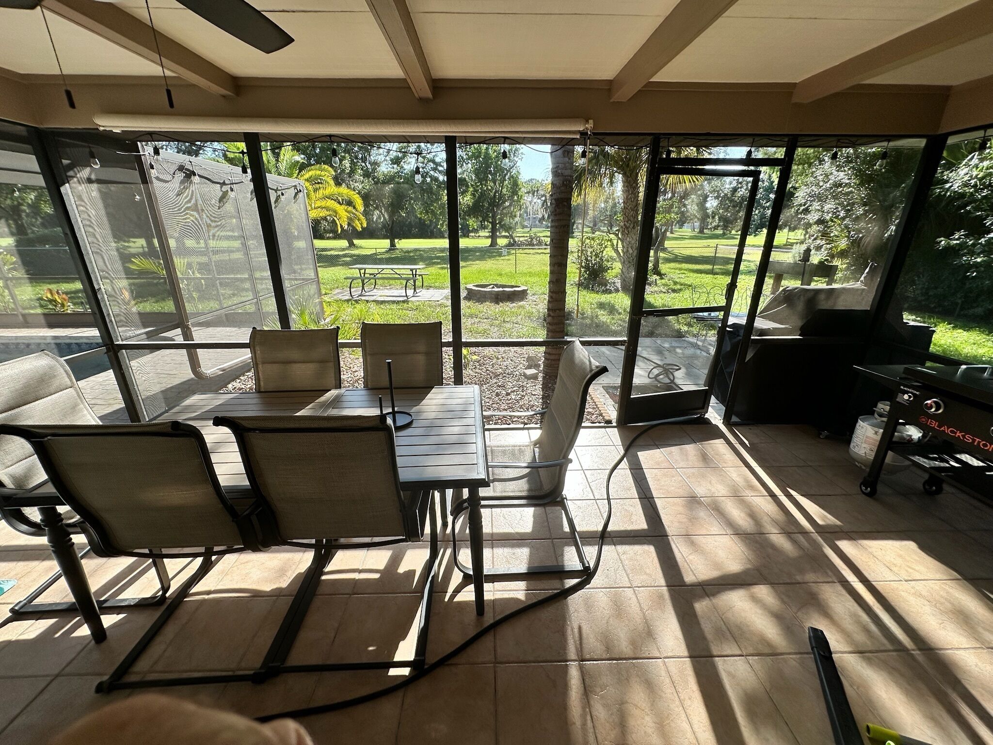 A sunlit patio with a table and chairs, a grill, and a view of a landscaped garden.
