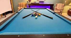 A pool table with balls and cues, surrounded by striped chairs and a table lamp. - Private Pool • Game Room • Fire Pit • Boat Parking (Crystal River)