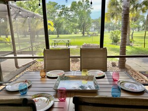 A dining area with a view of a park, featuring a table set with plates, glasses, and a tray. - Private Pool • Game Room • Fire Pit • Boat Parking (Crystal River)