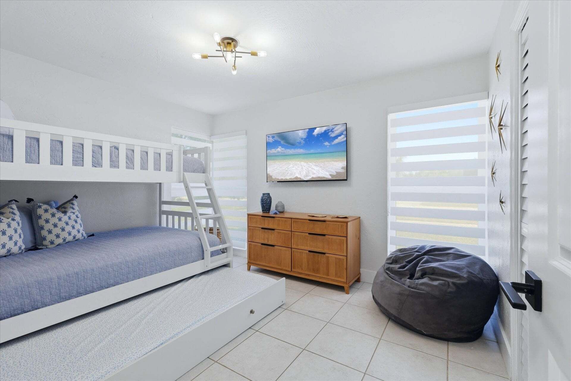 A child's bunk bed with a ladder, a wooden dresser, a bean bag chair, and a beach-themed wall hanging.