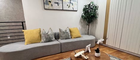 A modern living room with a grey sofa, a round wooden coffee table, and a large plant.