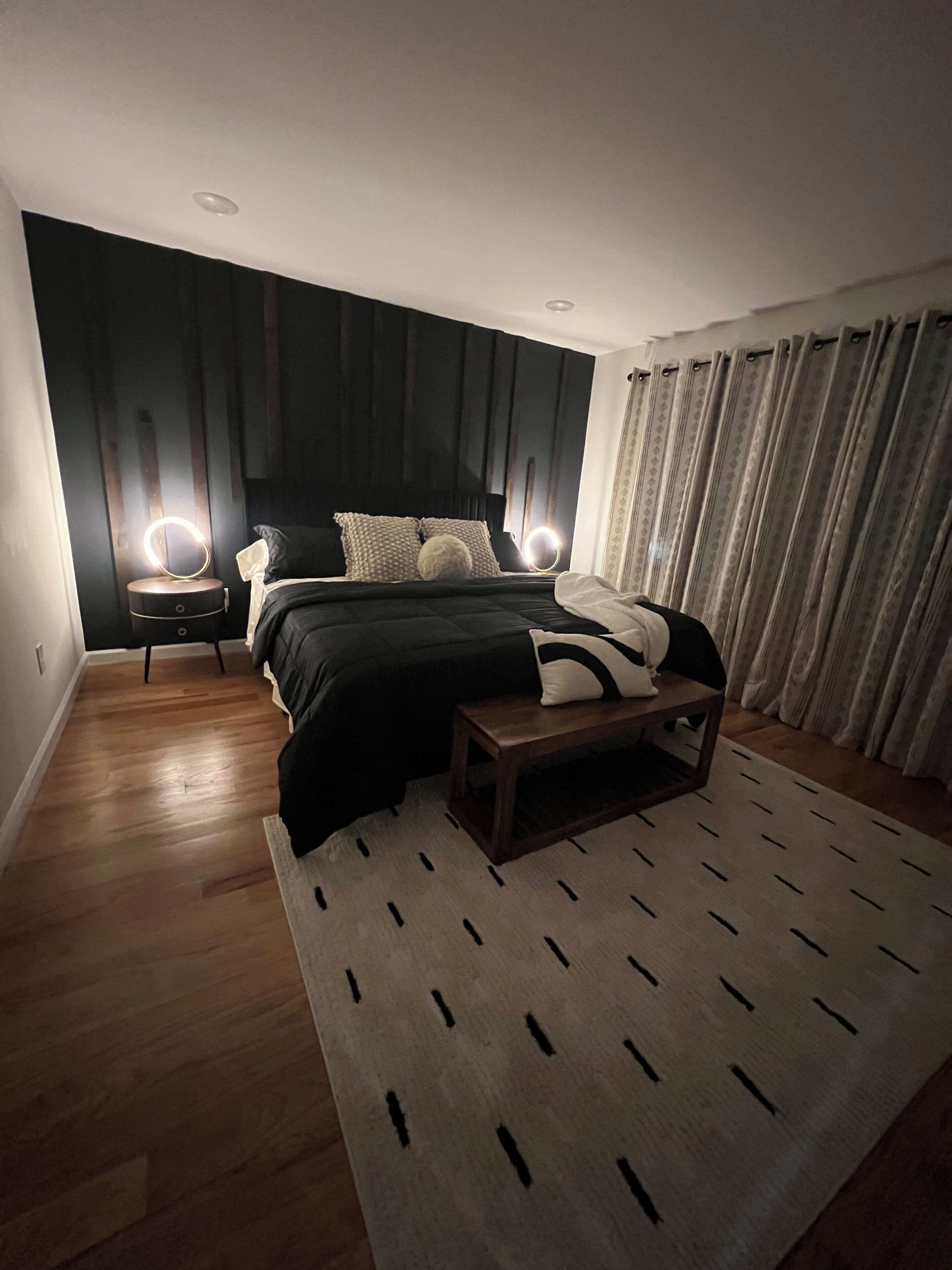 Een moderne slaapkamer met een groot bed, nachtlampjes, een houten vloer en een kamerbreed tapijt met een patroon.