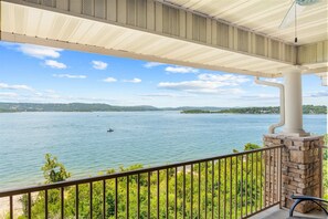 A covered balcony with a view of a lake, a boat, and distant hills. - Club Yakov & 3BDR Lakefront (Hollister)