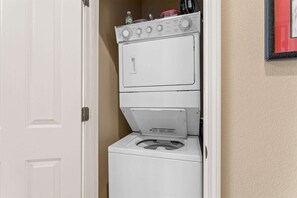 A stacked washer and dryer unit in a small laundry room with a white door and beige walls. - Club Yakov & 3BDR Lakefront (Hollister)