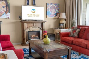 Ein Wohnzimmer mit Kamin, einem darüber montierten Fernseher, einem roten Sofa und einem Couchtisch mit einer Vase.