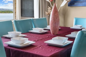 A dining table set with white plates and bowls, a vase with red and white stripes, and teal chairs. - Club Yakov & 3BDR Lakefront (Hollister)