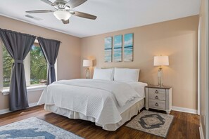 A bedroom with a bed, nightstands, lamps, a ceiling fan, and artwork on the wall. - Bluff Villa in Sea Pines Near South Beach Marina, Tennis, Pickleball & Golf (Hilton Head Island)