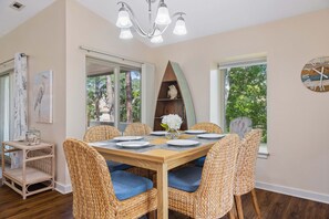 A dining area with a round table, wicker chairs with blue cushions, a chandelier, and a clock on the wall. - Bluff Villa in Sea Pines Near South Beach Marina, Tennis, Pickleball & Golf (Hilton Head Island)