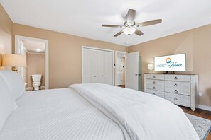 Une chambre à coucher avec un lit, un ventilateur de plafond, une télévision et une commode.