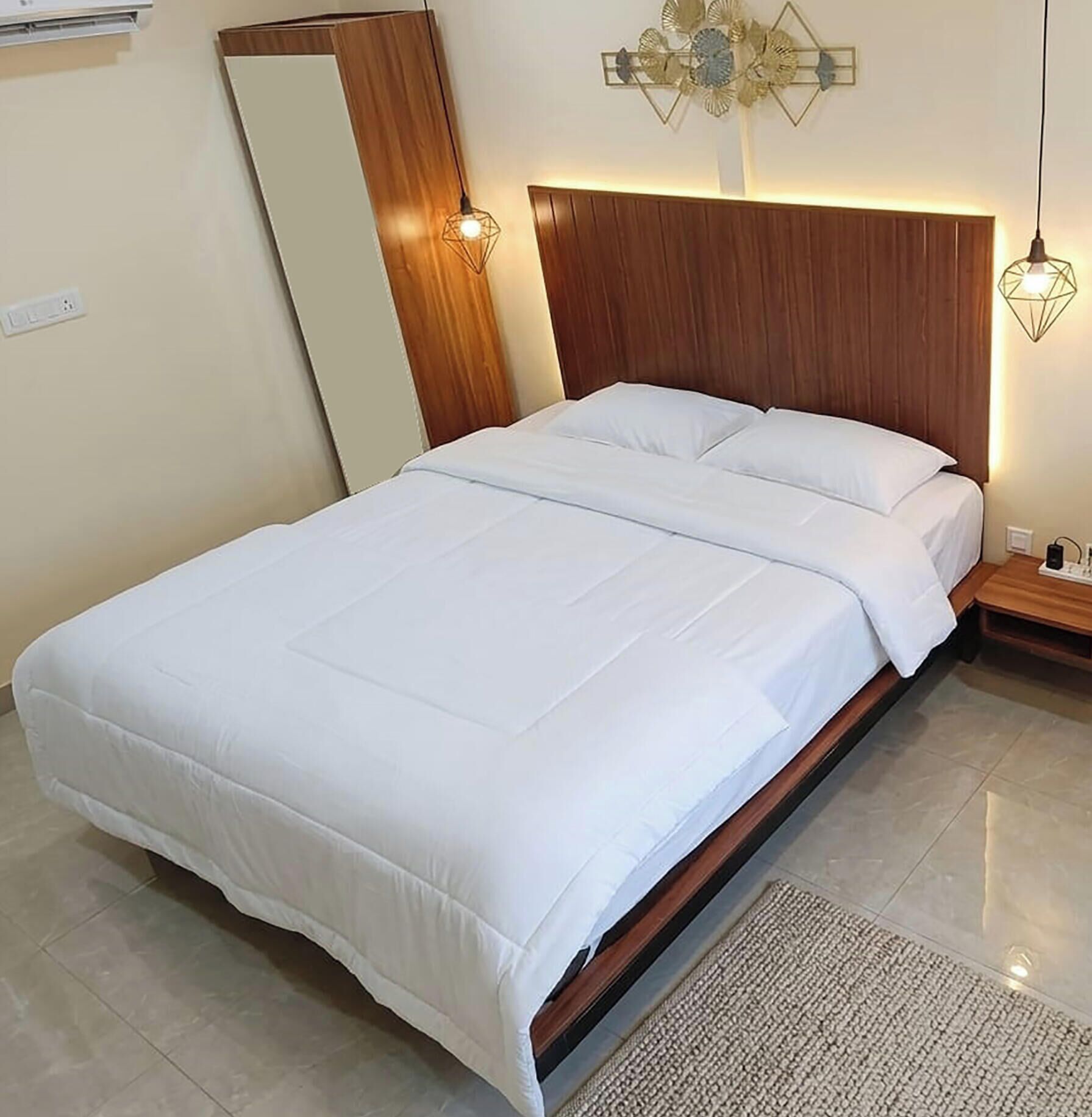A neatly made bed with white linens in a room with a wooden headboard and a wall-mounted light fixture.