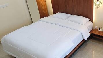 A neatly made bed with white linens in a room with a wooden headboard and a wall-mounted light fixture.
