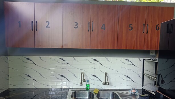 A kitchen with numbered wooden cabinets, a marble backsplash, and a stainless steel sink. - Umah Delod Dangin (Ubud)