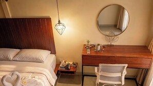 A bedroom with a wooden headboard, a bed with white bedding, a bedside table with a lamp, a mirror, and a desk with a chair. - Umah Delod Dangin (Ubud)