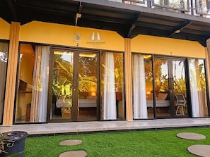 A guest house with large sliding glass doors, a balcony, and a well-maintained lawn.