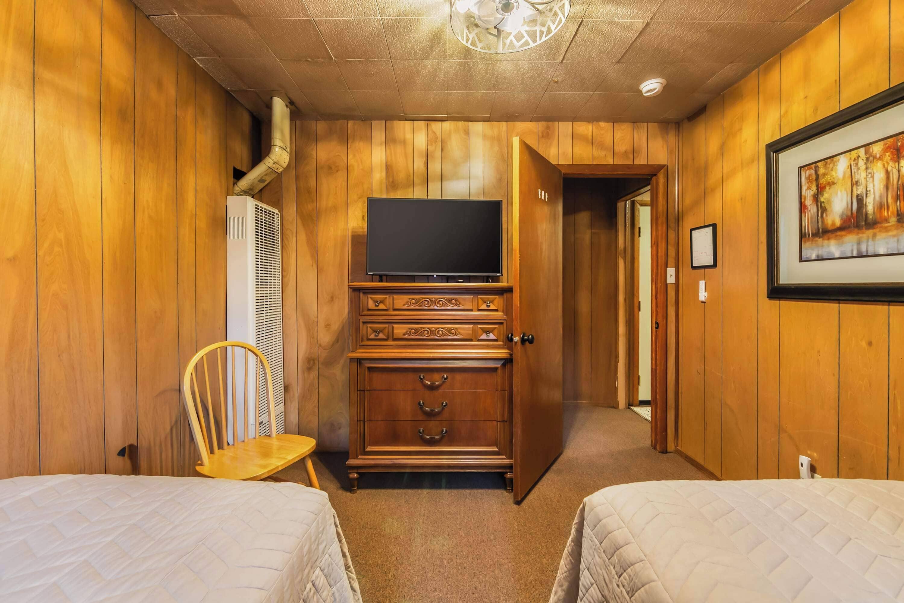 A room with wooden walls, a television on a cabinet, a chair, and two beds.