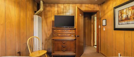 A room with wooden walls, a television on a cabinet, a chair, and two beds.