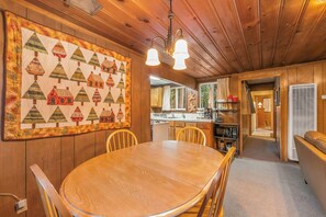 Ein Holzinterieur mit Esstisch, Stühlen, einer Küchenzeile und einer großen Stegdecke an der Wand.