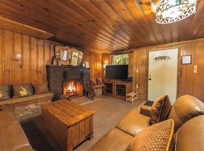 Ein gemütliches Wohnzimmer mit Kamin, Ledersofa, Couchtisch aus Holz und Fernseher.