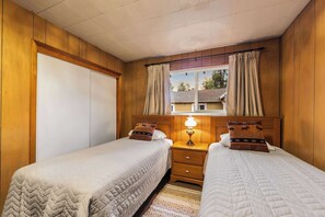 A room with two beds, wooden walls, a window with curtains, and a bedside lamp. - Paradise Bungalow - Cozy Cabin Escape (South Lake Tahoe)