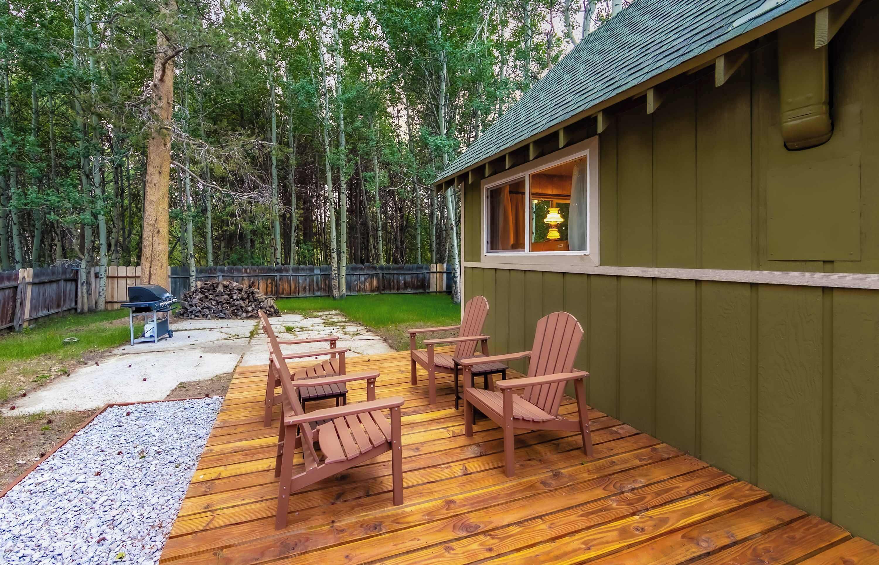 Eine Holzterrasse mit Adirondack-Stühlen und einem Grill.