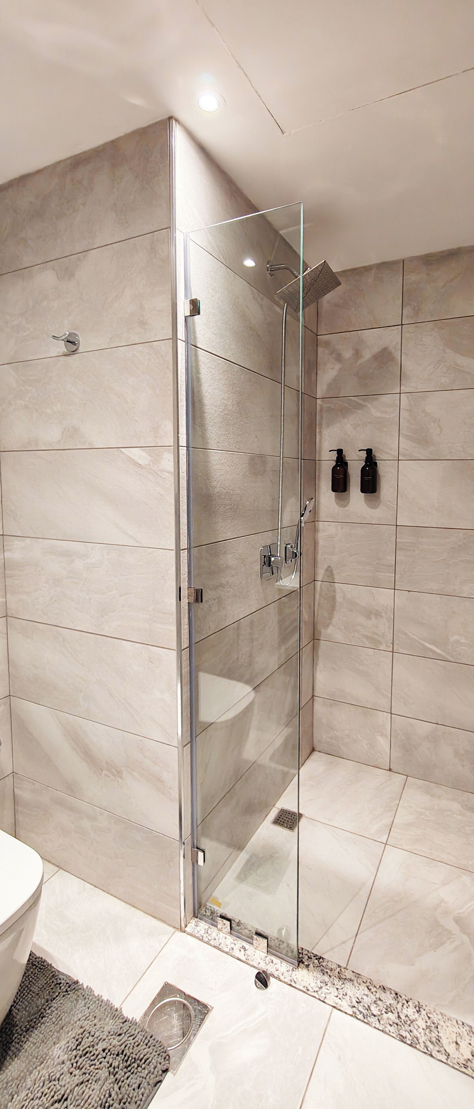 A modern bathroom with a glass-enclosed shower, marble walls, and a sink with two soap dispensers.