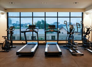 Ein Fitnessstudio mit Laufbändern und Ergometer, großen Fenstern mit Blick auf die Stadt und einem hellen, modernen Ambiente.
