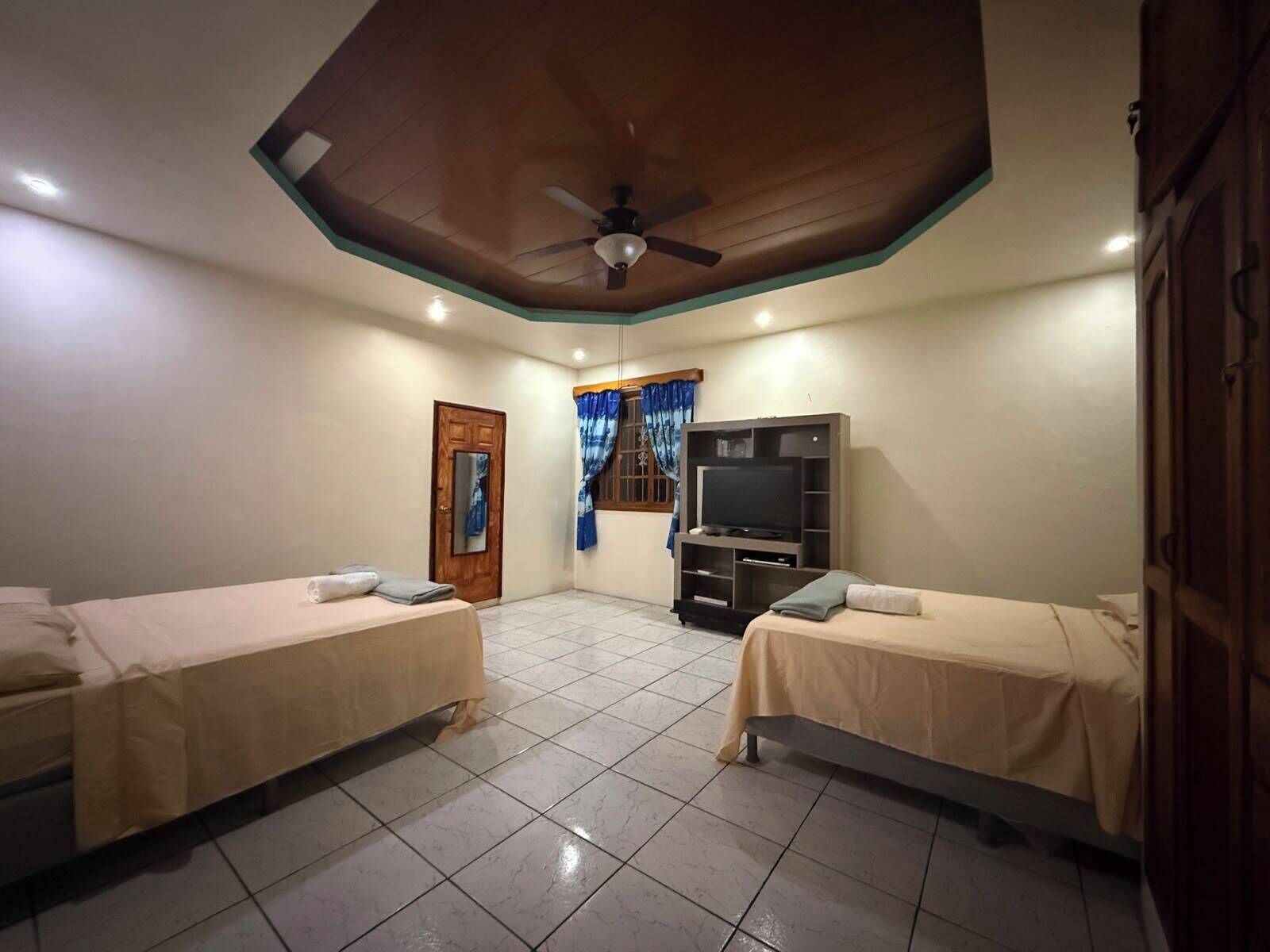 A room with two beds, a ceiling fan, a television, and a door.