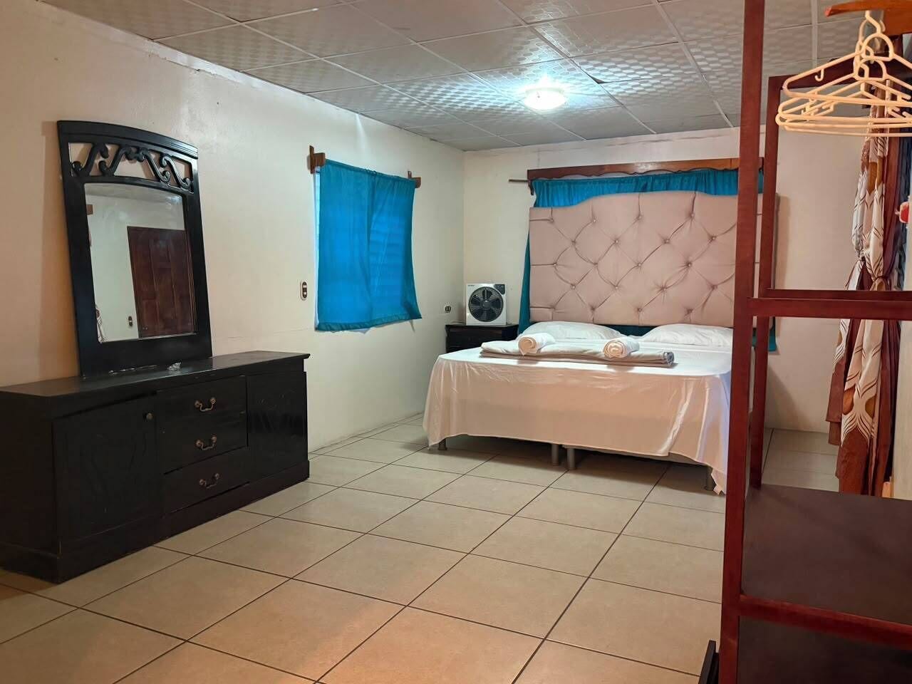 A bedroom with a bed, a dresser, a mirror, and a fan.