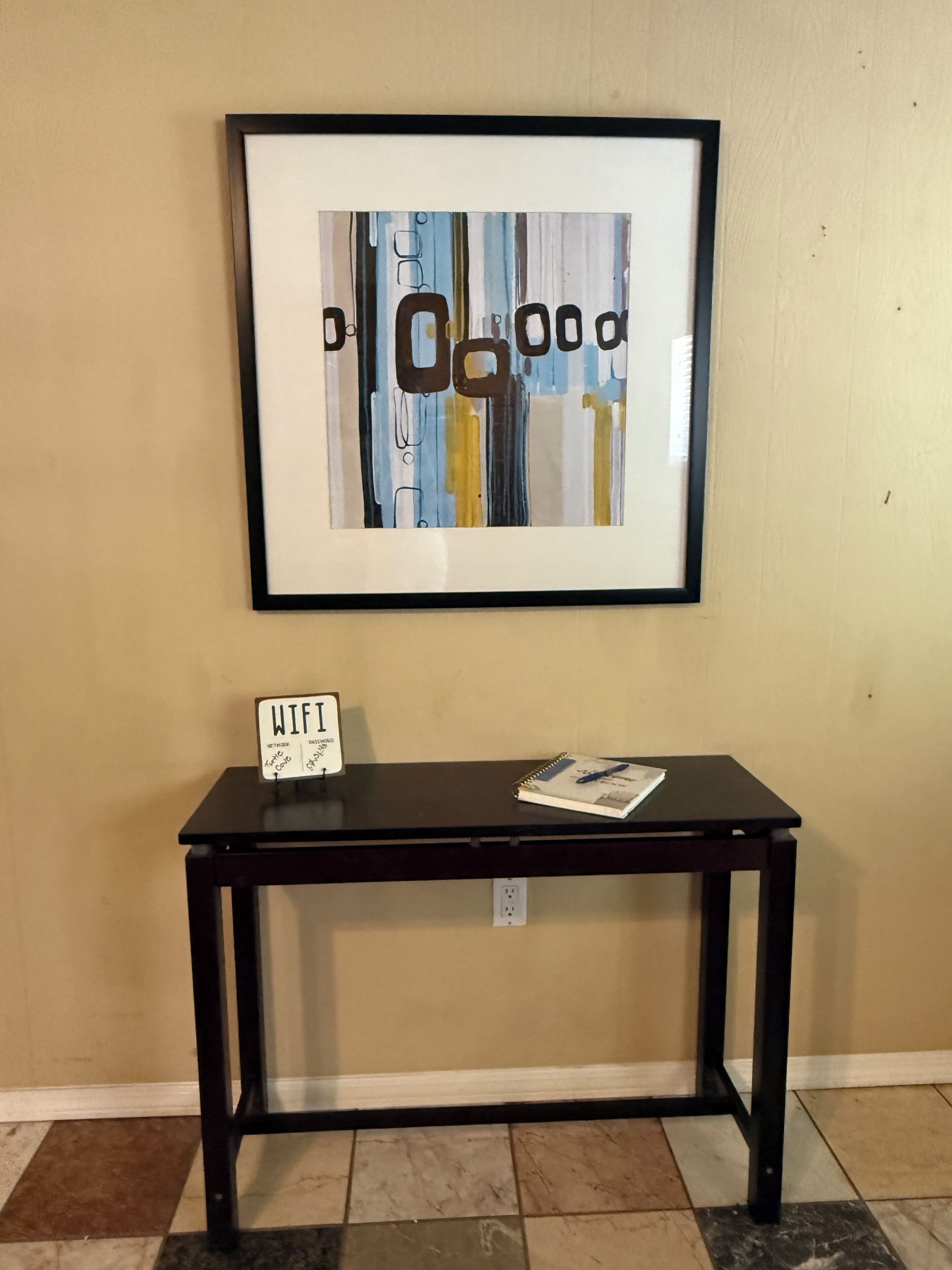 A framed artwork on a wall above a black table with a sign indicating WiFi availability.