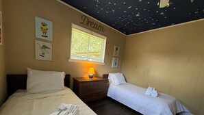 Hotellihuone, jossa on kaksi sänkyä, yöpöytä lampun kanssa ja ikkuna, jossa on sälekaihtimet.
