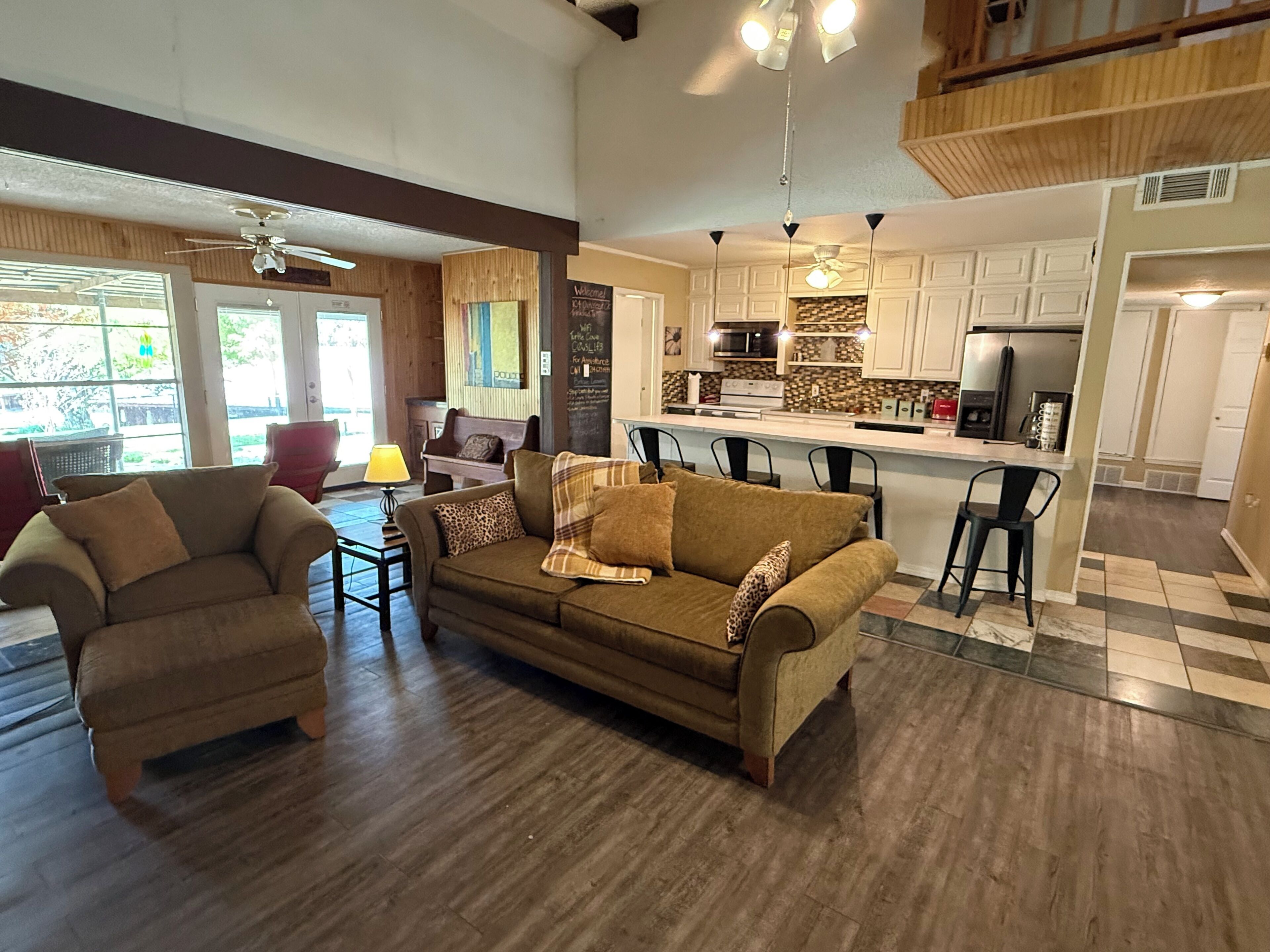 Una sala de estar moderna con un sofá y sillones, un comedor con mesa y sillas, y una cocina con una isla central.