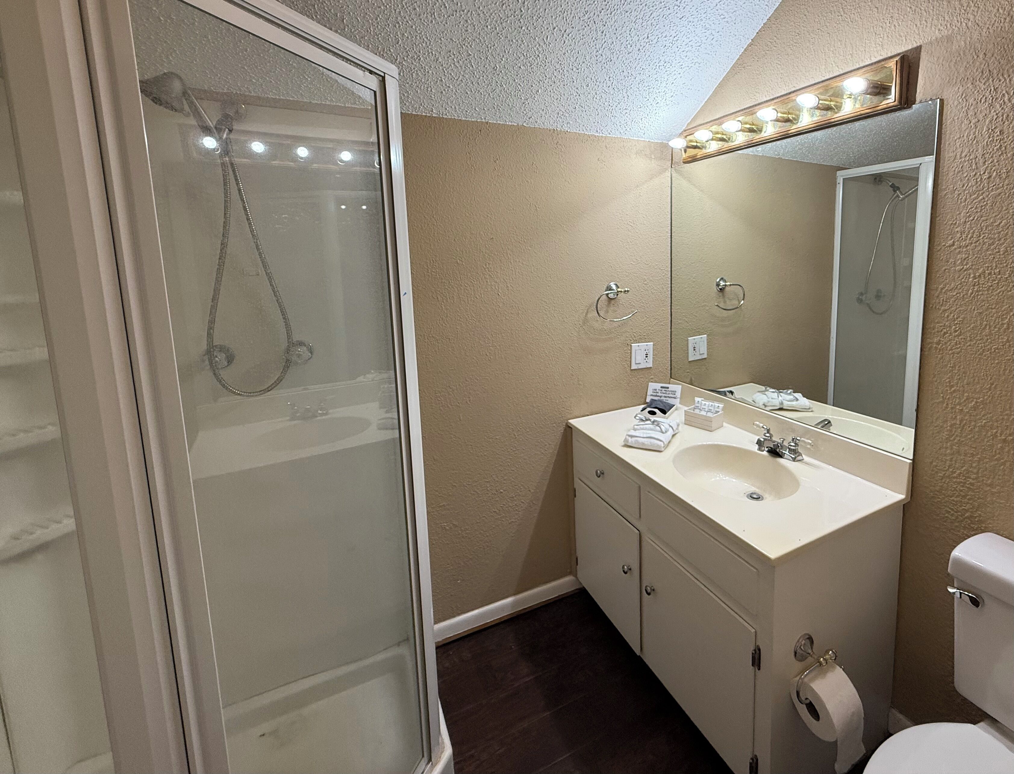 Un baño con cabina de ducha de vidrio, lavamanos con espejo y retrete.