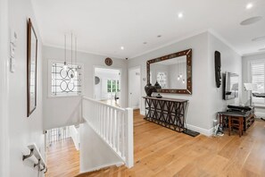 A spacious hallway with a wooden floor, a white railing, and a decorative console table. - Spacious Parnell Home at Auckland Domain by Zodiak (Auckland City)