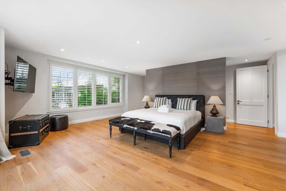 A bedroom with a bed, bedside lamps, a suitcase, and a window with blinds.