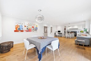 A spacious living area with a dining table, white chairs, a grey sofa, and a kitchen in the background. - Spacious Parnell Home at Auckland Domain by Zodiak (Auckland City)