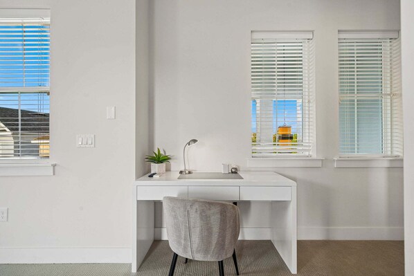 A minimalist office space with a white desk, a grey chair, and two windows with blinds. - The Reserve at Reunion-TT491 (Kissimmee)