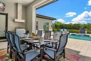 An outdoor dining area with a pool and lounge chairs in the background. - The Reserve at Reunion-TT491 (Kissimmee)