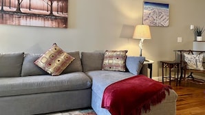 A living room with a grey sofa, patterned throw pillows, a red throw blanket, a lamp, and two wall-mounted paintings. - Amazing Mountain Views, Walk to BMR & Downtown! (Banner Elk)