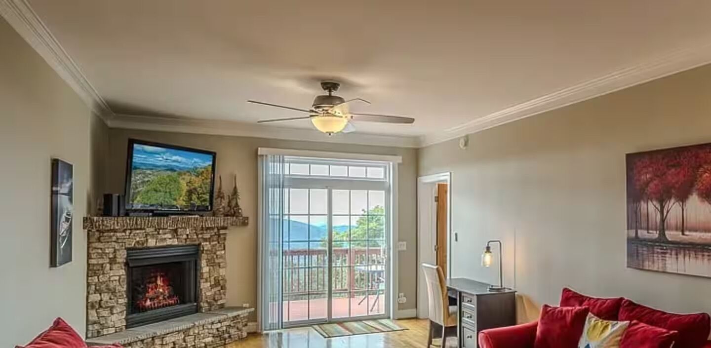 A living room with a stone fireplace, a ceiling fan, a television, and a red couch.
