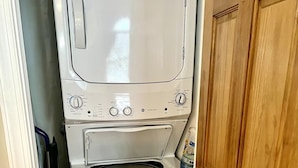 A compact, white washer and dryer unit with a front-loading design, located in a small laundry room with wooden flooring and a wooden door. - Amazing Mountain Views, Walk to BMR & Downtown! (Banner Elk)