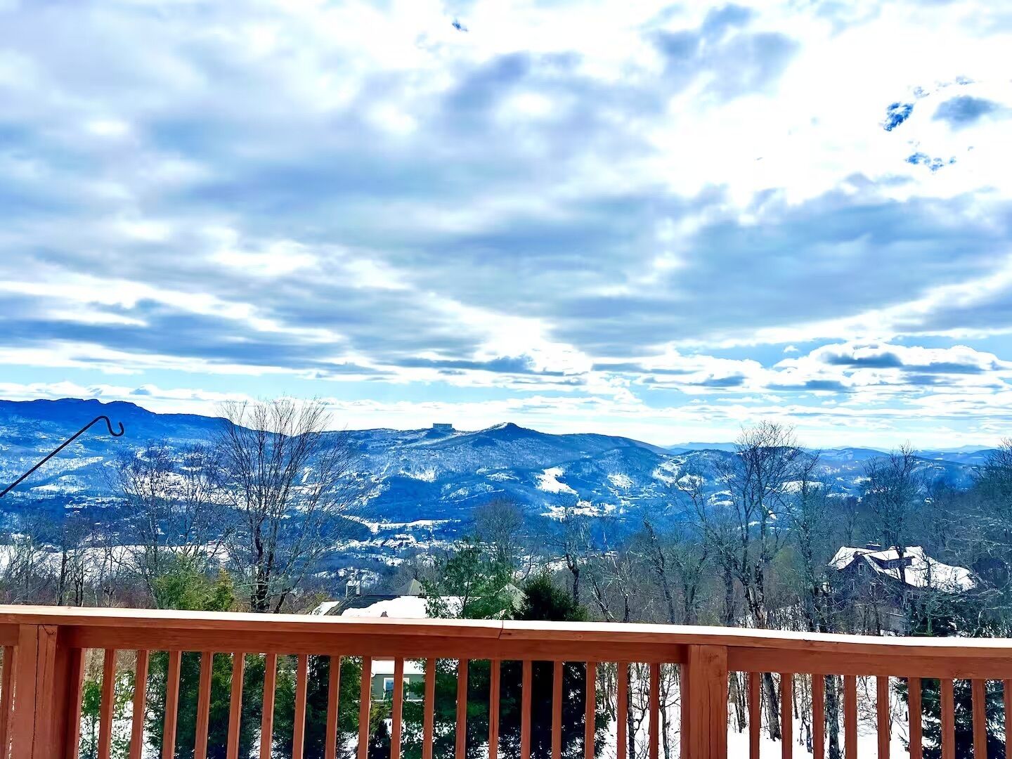 A wooden deck with a view of snow-covered mountains and a partly cloudy sky.