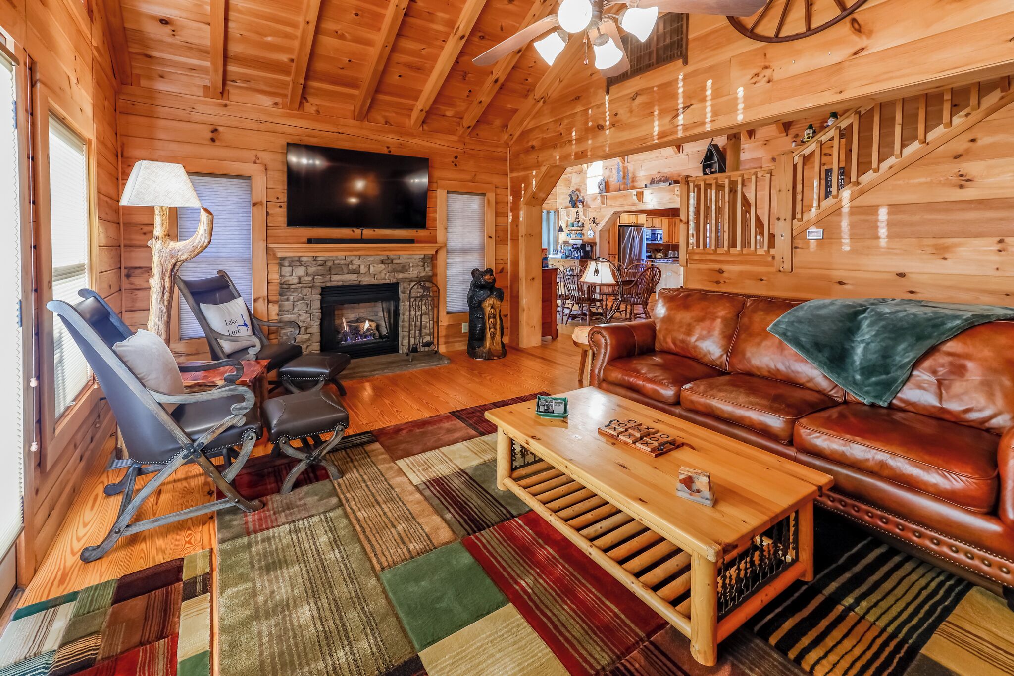 A cozy log cabin interior with a fireplace, leather sofa, and a television mounted on the wall.
