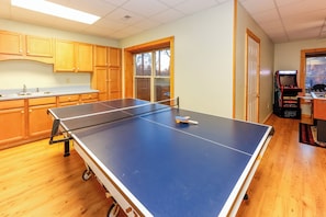 Une pièce avec une table de ping-pong, des meubles en bois, une fenêtre et une borne d’arcade.