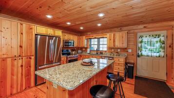 A wooden cabin interior with a kitchen featuring a stainless steel refrigerator, a microwave, and a granite countertop.