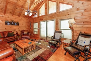 A log cabin interior with a fireplace, leather furniture, and large windows. - Game Room / Mtn Views / Hot Tub / Fire Pit & Fire Table / Coffee Bar / (Lake Lure)
