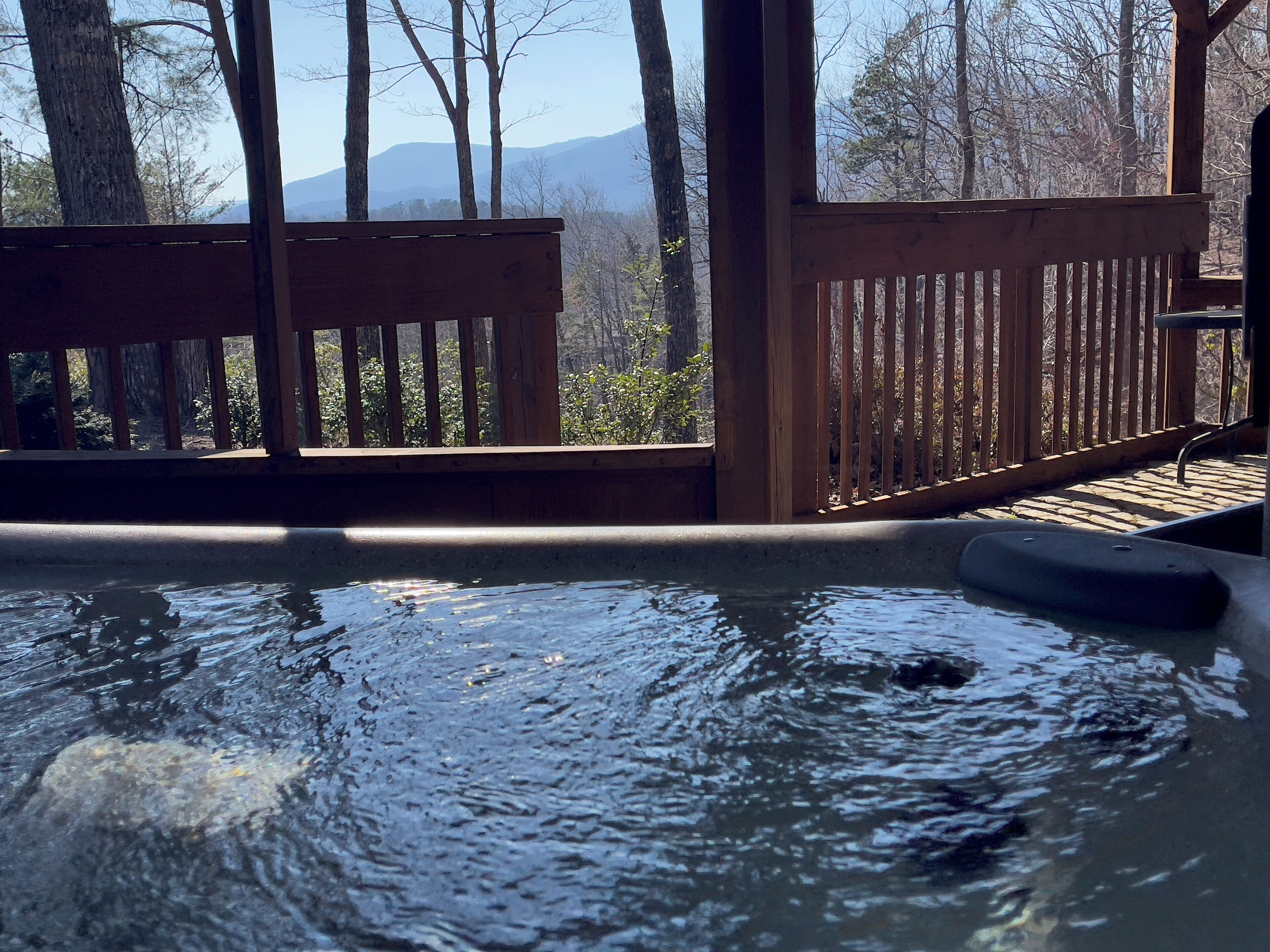 Un jacuzzi con cubierta de madera, rodeado de árboles y vistas a la montaña.