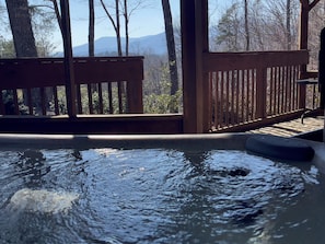 Un bain à remous doté d’une terrasse en bois, entouré d’arbres et offrant une vue sur la montagne.