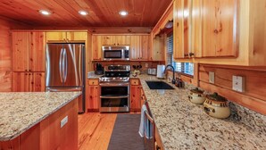 A kitchen with wooden cabinets, stainless steel appliances, granite countertops, and a window with blinds. - Game Room  / Mtn Views  / Hot Tub / Fire Pit & Fire Table /  Coffee Bar / (Lake Lure)